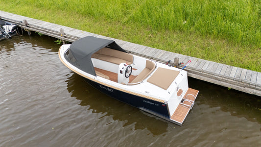 Reitdieper 570 Tendersloep aangemeerd aan een steiger, met zwarte kap en comfortabele zitbanken, perfect voor recreatief gebruik op het water.