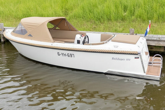 Zijaanzicht van de Reitdieper 570 Tendersloep met zwarte romp en beige kussens, liggend aan een houten steiger in een rustige gracht.